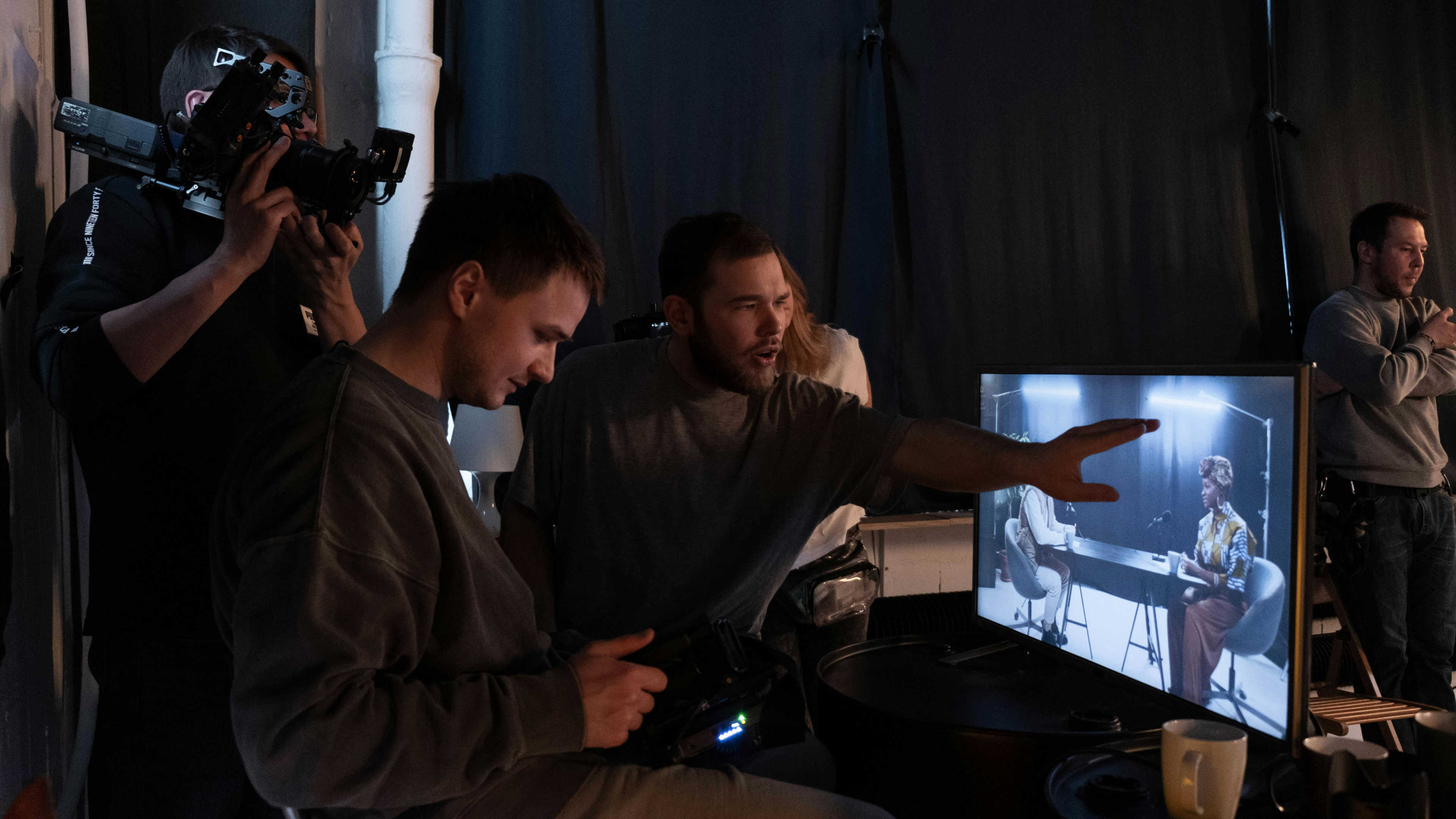 A director pointing at a screen, with a cameraman behind him and assistant reviewing video footage