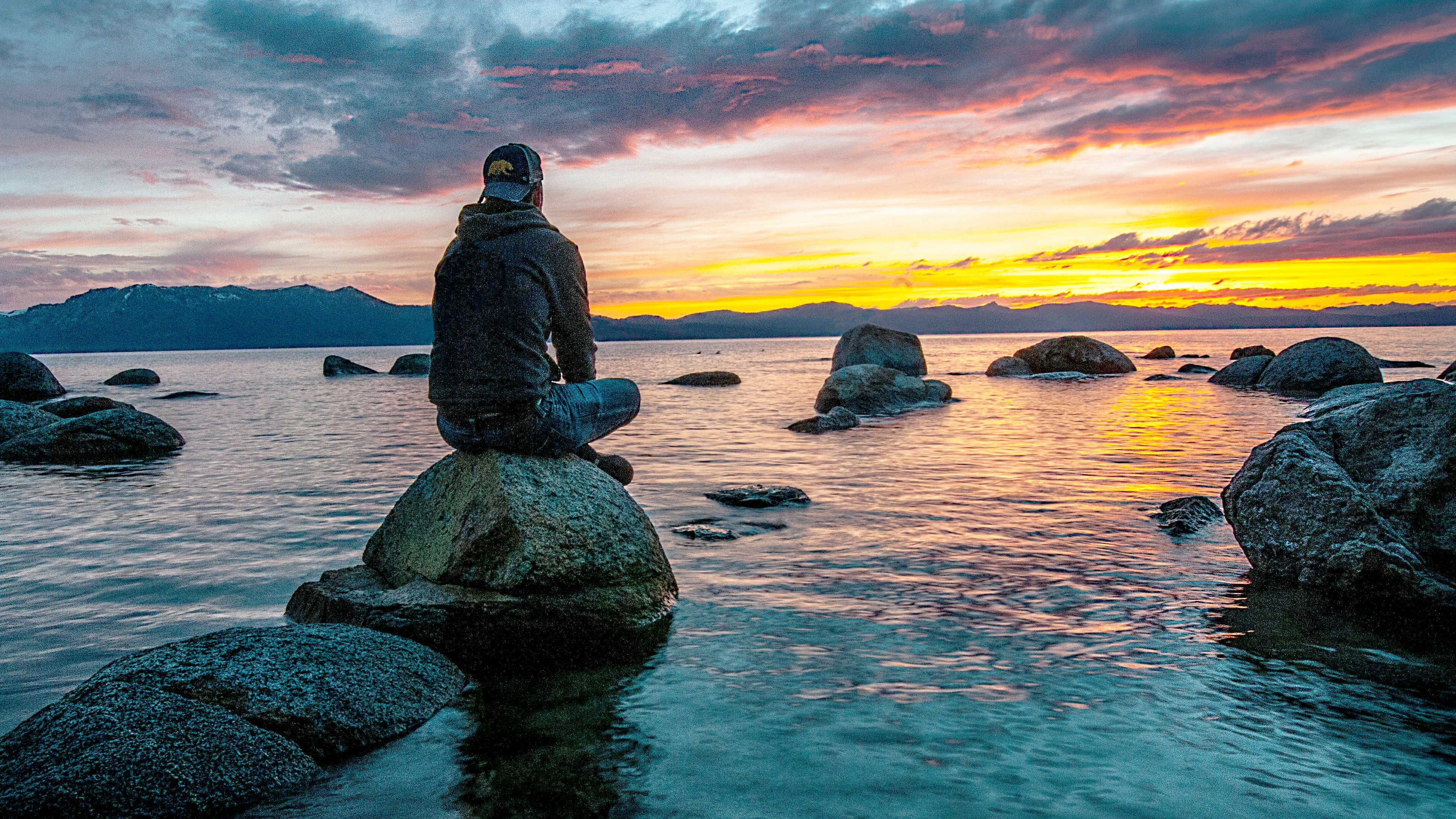 A man sitting on the rocks watching sunset over the water