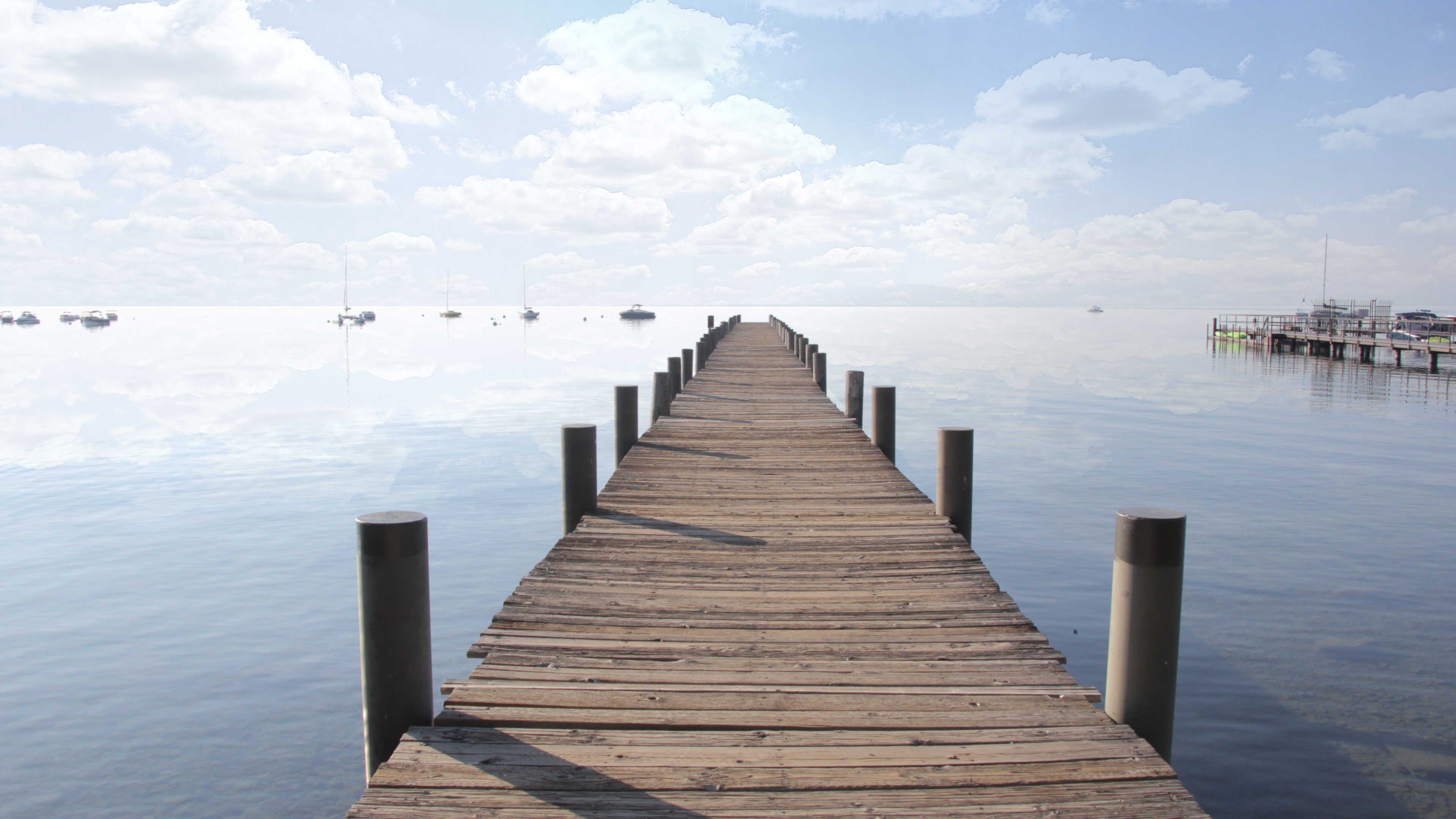 A pier on Lake Tahoe extending into the distance with the sky reflecting on the surface of the lake
