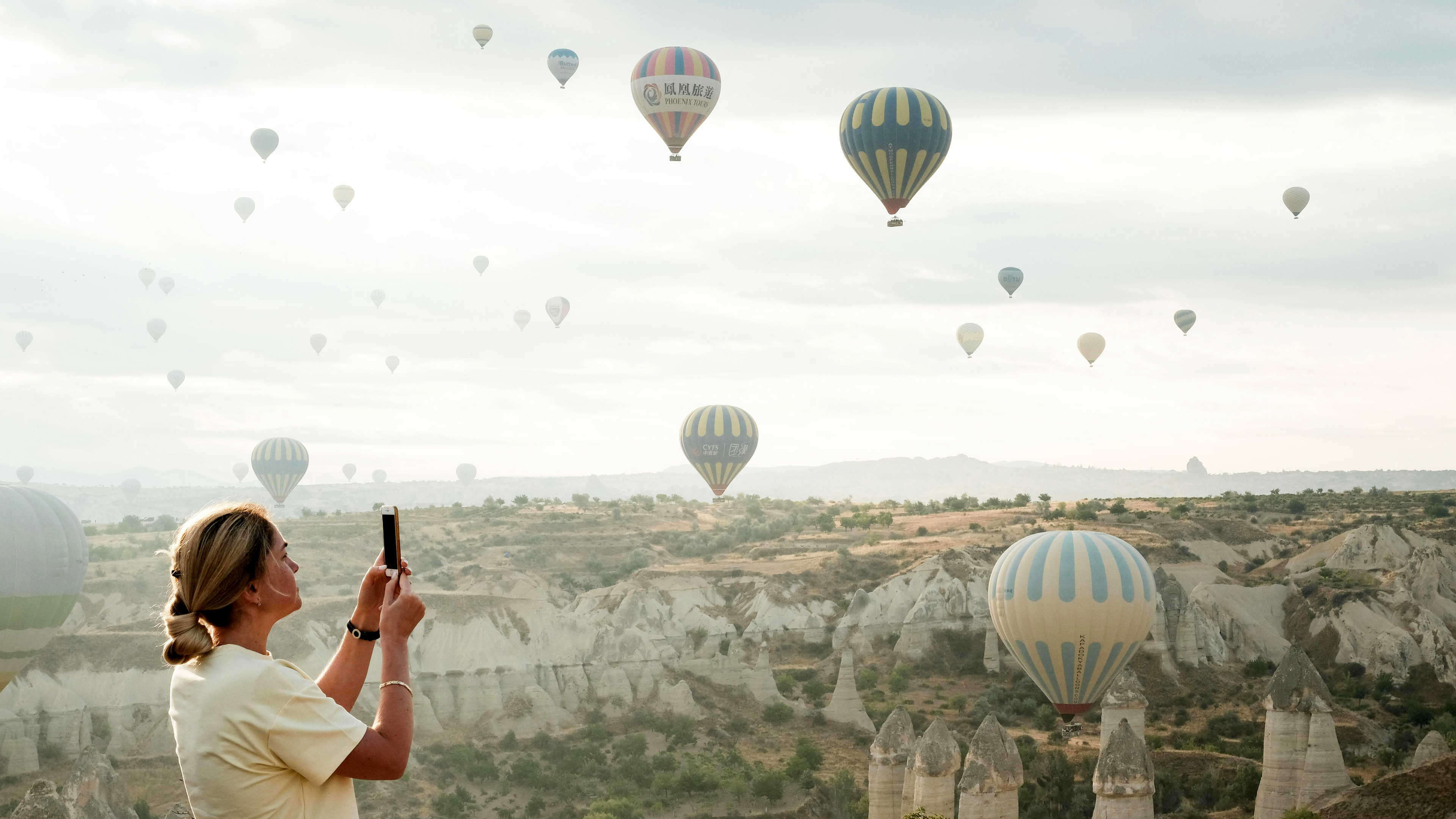 A woman taking a photo of hot air balloons over a landscape