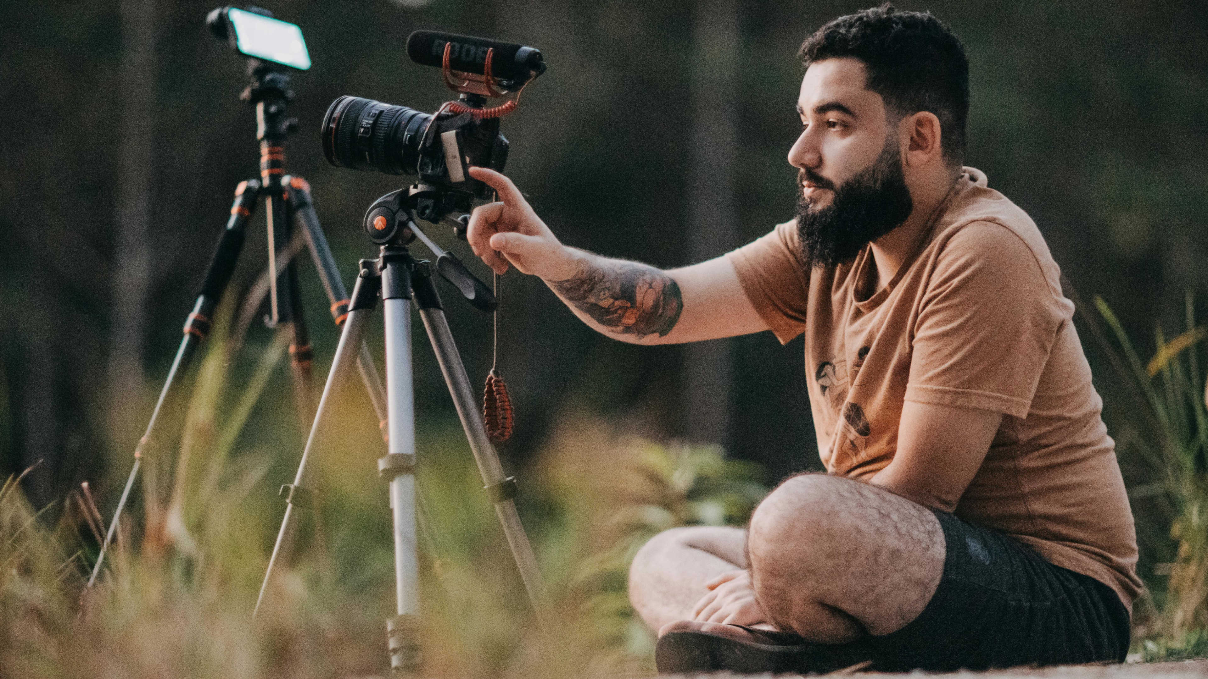 A man sitting on the ground adjusting his camera on a tripod