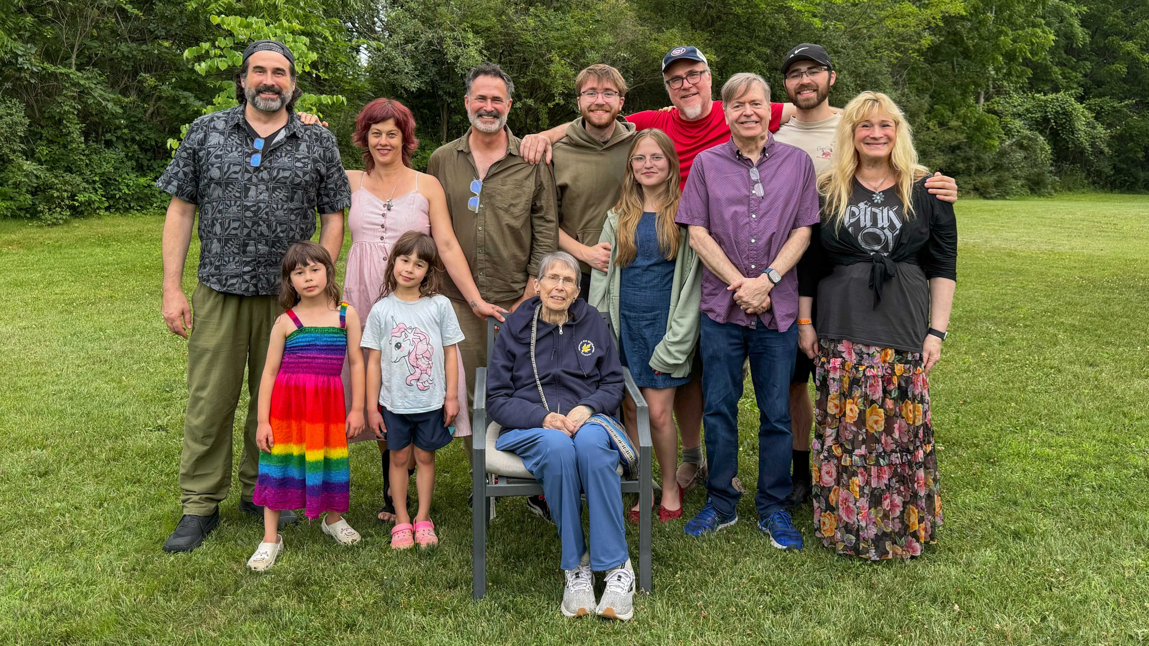 Multigenerational family group posing together on a lawn surrounded by trees.