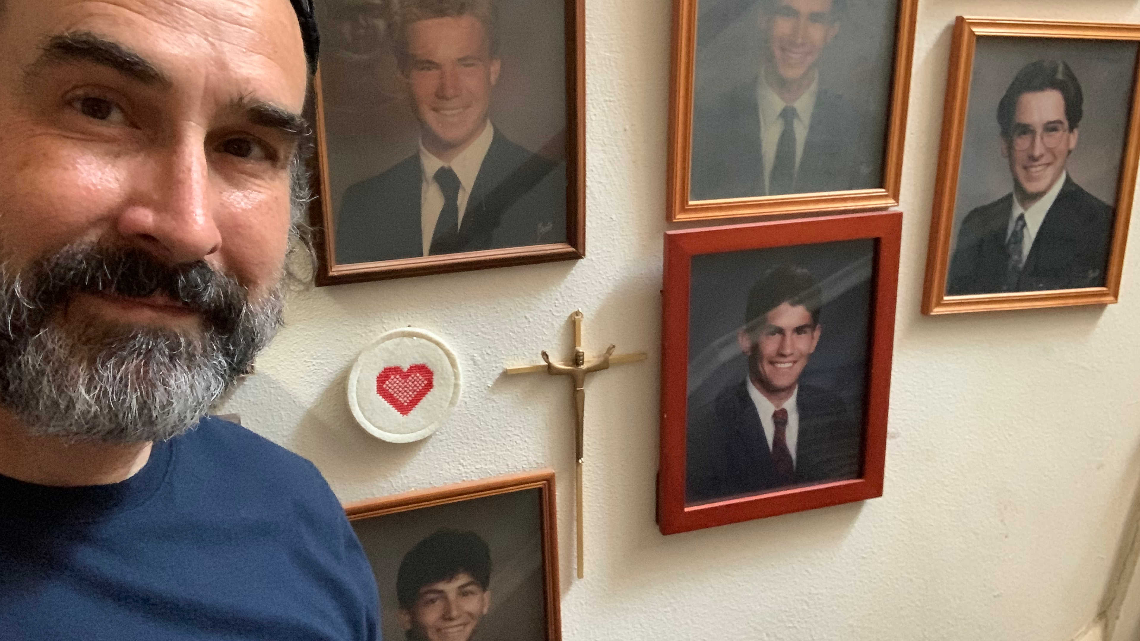 Selfie beside a stairwell display of framed portraits of family.