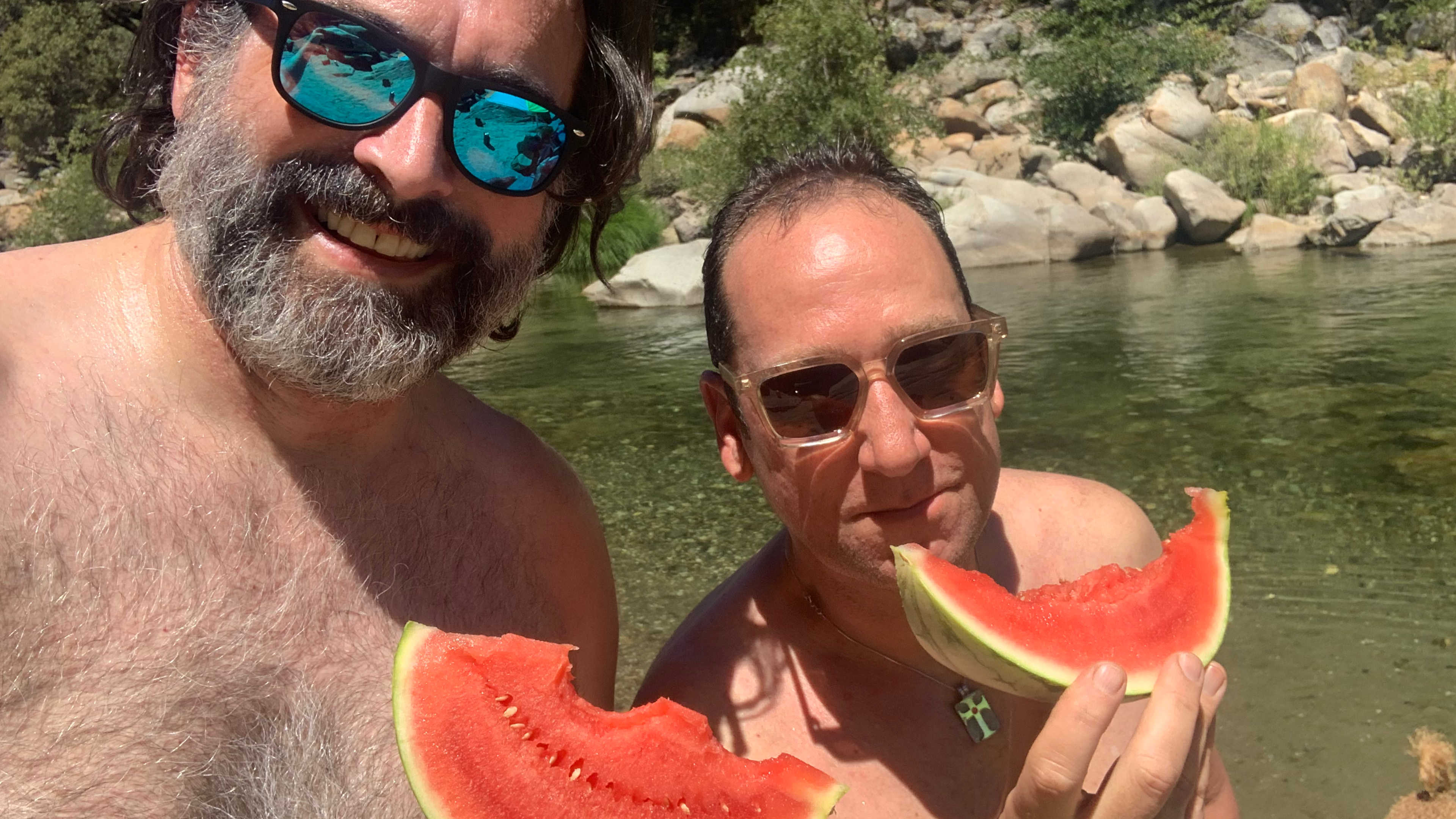 Me and a friend holding watermelon slices while standing in the South Yuba River.