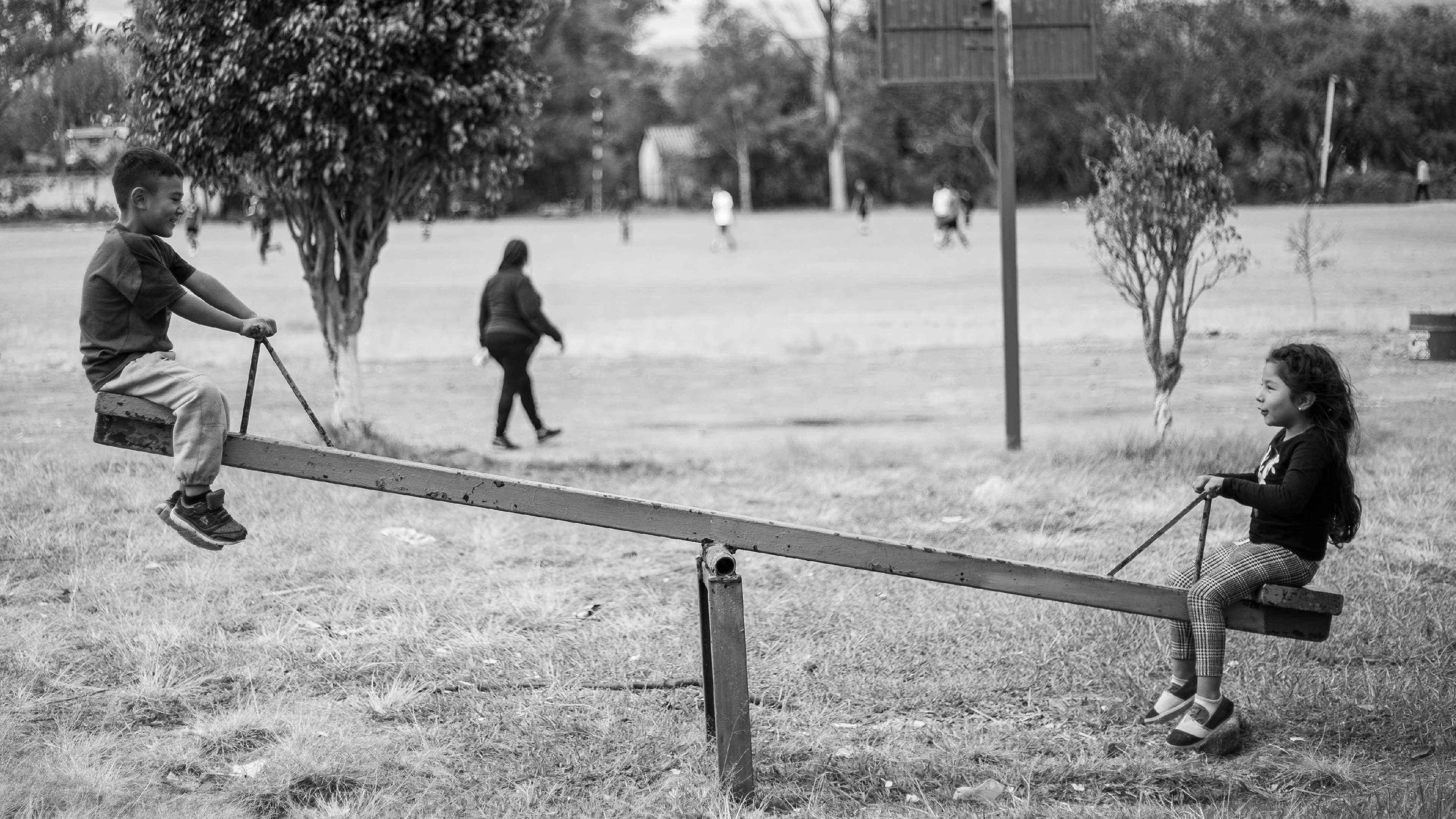 Black & white editorial photograph of children on a seesaw in a park.
