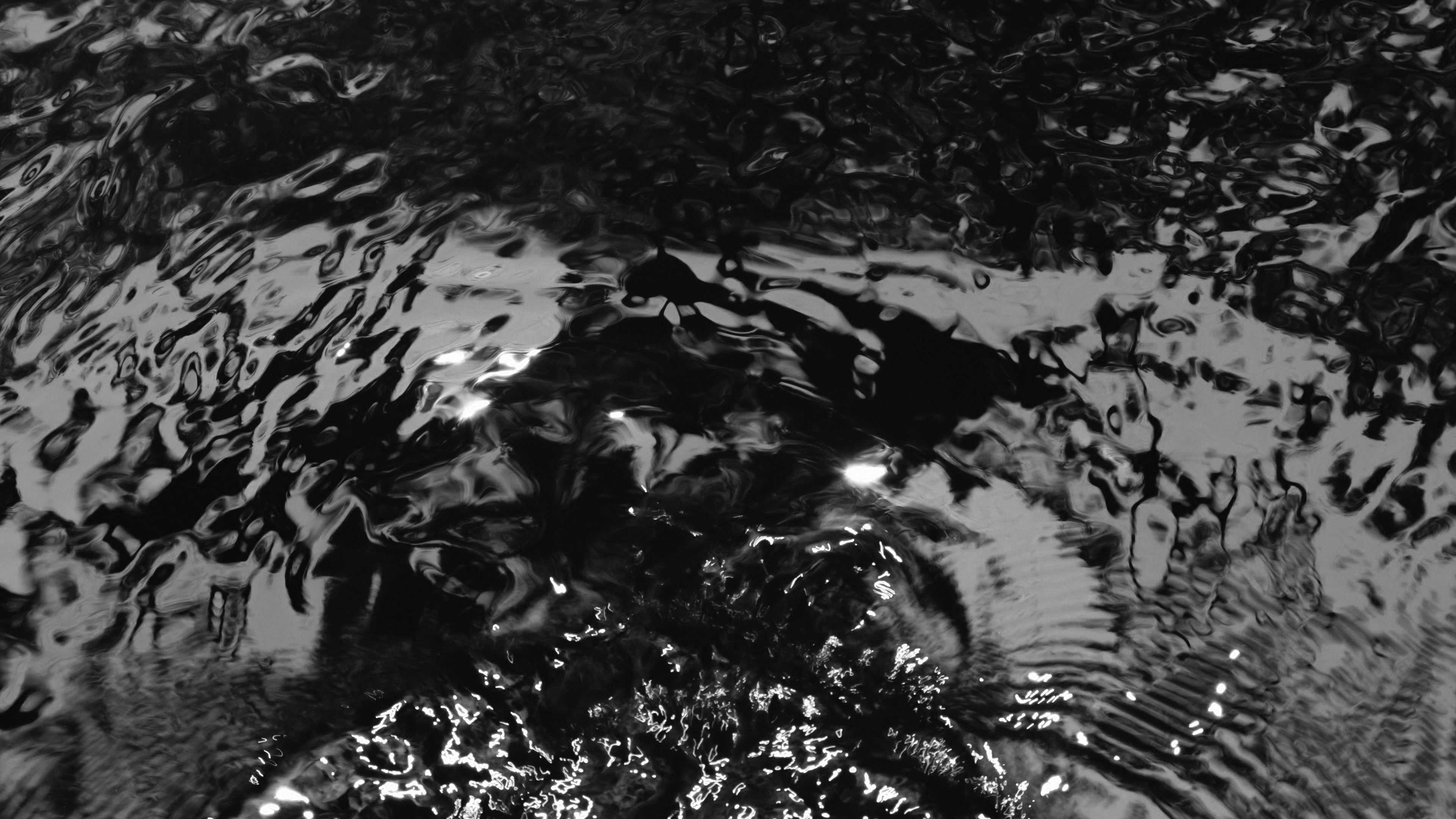 Editorial black and white image of dark water with waves disrupting the surface.